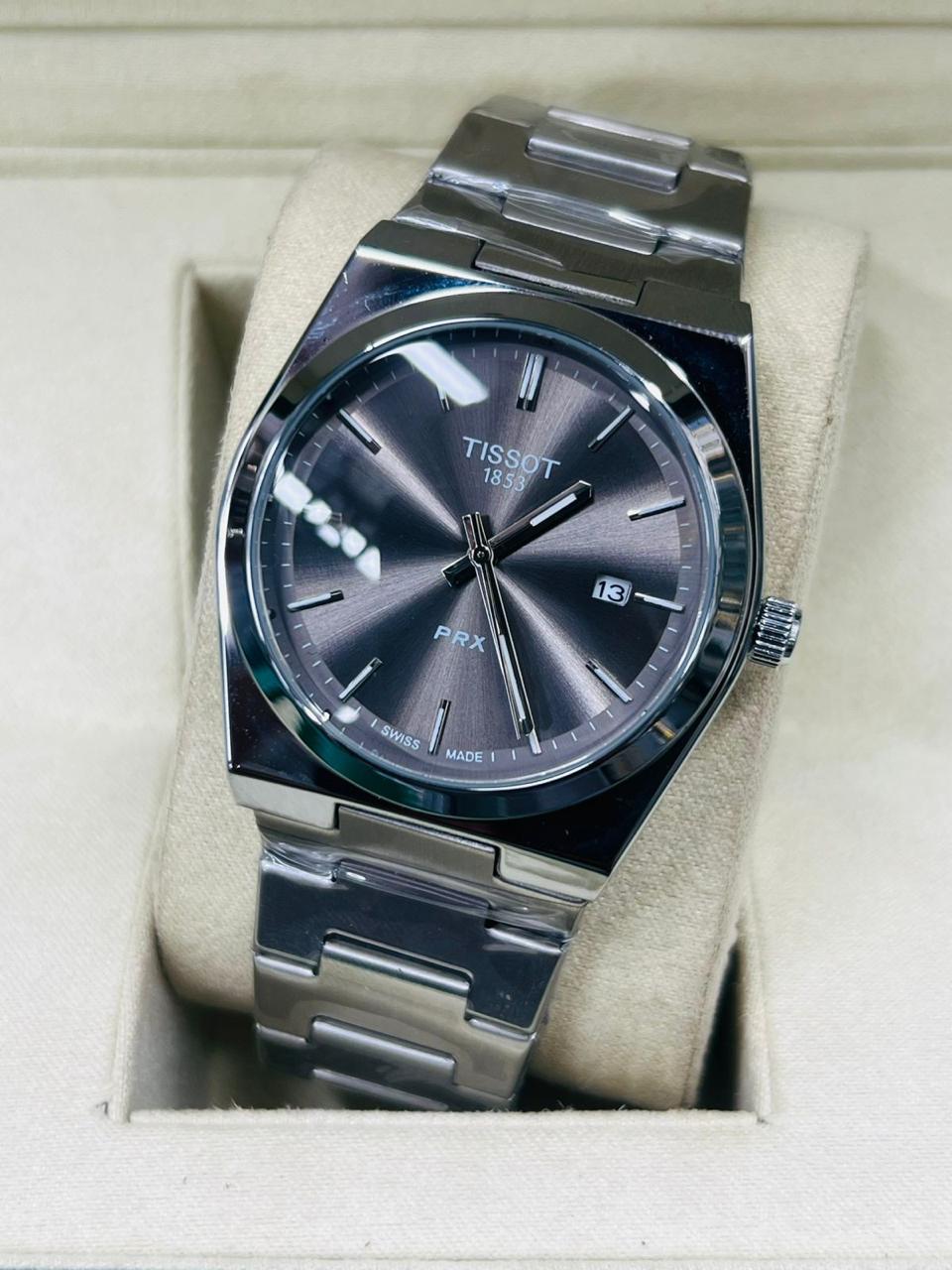 Tissot watch with silver metal band and dark face in a beige box